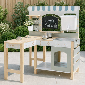 L-shaped wooden café play kitchen with mint green accents, chalkboard sign, and striped awning on patio